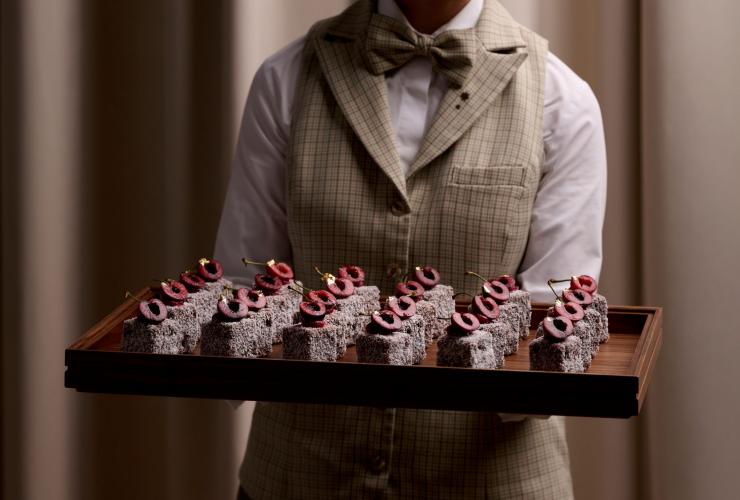 新南威尔士州，悉尼，桥街，The Lands by Capella，服务人员手托一盘精致高档的拉明顿蛋糕 © Esteban La Tessa 251201 The Lands by Capella F&B Shoot5620 版权所有