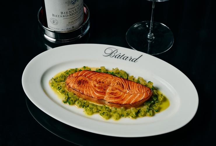 带 Bâtard 标记的盘子里盛着油封三文鱼配蔬菜丁，旁边放着一瓶葡萄酒。© Maison Bâtard 版权所有