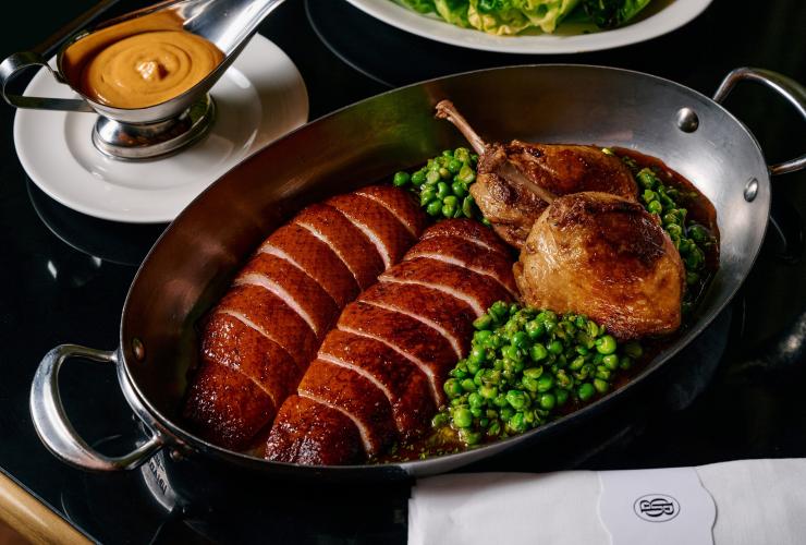 黑色餐桌上摆放着一盘烤鸭胸与鸭腿配豌豆，以及一个酱汁碟。© Pete Dillon 版权所有