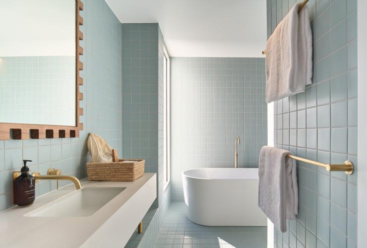 卫生间内景，墙面铺设蓝色方块瓷砖，左侧是洗手台和镜子，另有一个独立浴缸。© Shot By Thom 版权所有