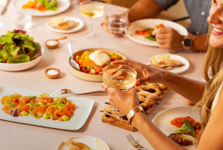 摆放着美食的餐桌，一位女性手握玻璃杯。© Saltbox 版权所有